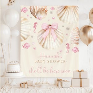 Może przedstawiać: Baner na baby shower z motywem muszli. Baner zawiera ilustracje muszli, koników morskich i ryb w odcieniach różu i beżu. Tekst "Hannah's BABY SHOWER she'll be here soon" jest wyświetlany w kolorze różowym.