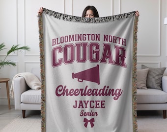 May include: White woven throw blanket with a maroon design. The design features the text "Bloomington North Cougar Cheerleading Jaycee Senior" with a maroon megaphone and a maroon bow.