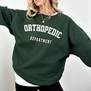 Könnte beinhalten: Ein dunkelgrüner Pullover mit dem Text "ORTHOPEDIC DEPARTMENT" in Weiß.