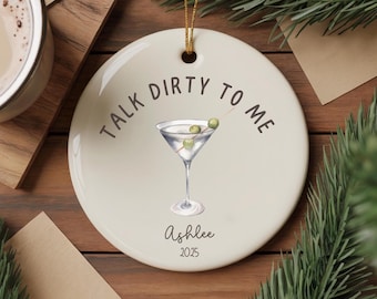 以下が含まれることがあります： クリーム色のセラミックオーナメント。マティーニのイラストと「Talk Dirty To Me」の文字。マティーニグラスにはオリーブが入っています。「Ashlee」という名前と「2025」の年号が下に印刷されています。