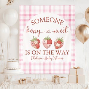 Könnte beinhalten: Ein Babyparty-Banner mit rosa und weißem Vichy-Muster. Auf dem Banner steht "Someone berry sweet is on the way" und es zeigt Erdbeer-Illustrationen. Die Szene umfasst Ballons, Geschenke und einen Kuchen.