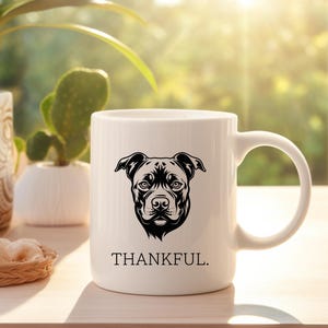 Pode incluir: Caneca de café de cerâmica branca com uma silhueta preta da cabeça de um pit bull e a palavra "THANKFUL." impressa na frente.