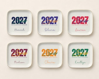 May include: Six square white ceramic trinket dishes with gold rims. Each dish features the text 2027, the word Senior in script, a team name like Bulldogs Cheer or Bruins Lacrosse, and a personalized name such as Hannah, Olivia, or Lauren.