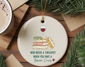May include: Round, white ceramic ornament with a gold string for hanging. The ornament features a stack of books, a wine glass, and the text "WHO NEEDS A THERAPIST WHEN YOU HAVE A Book Club ❤️".