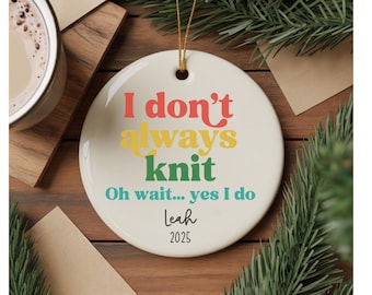 Pode incluir: Um enfeite redondo de cerâmica branca com o texto "I don't always knit" em vermelho, amarelo e verde. Abaixo, o texto diz "Oh wait... yes I do" em verde-azulado, com um nome e o ano de 2025. Uma corda dourada é anexada para pendurar.