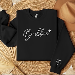 May include: Black sweatshirt with the word "Bubbie" written in white cursive with a small white heart to the right. The words "Sam Talia" are written in white on the left sleeve with a small white heart below.