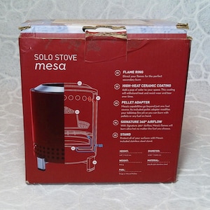 May include: A red box for a Solo Stove Mesa tabletop fire pit. The box features a diagram of the fire pit and lists features like a flame ring, high-heat ceramic coating, and pellet adapter. The box also lists the height as 17.27 cm and the diameter as 14.73 cm.