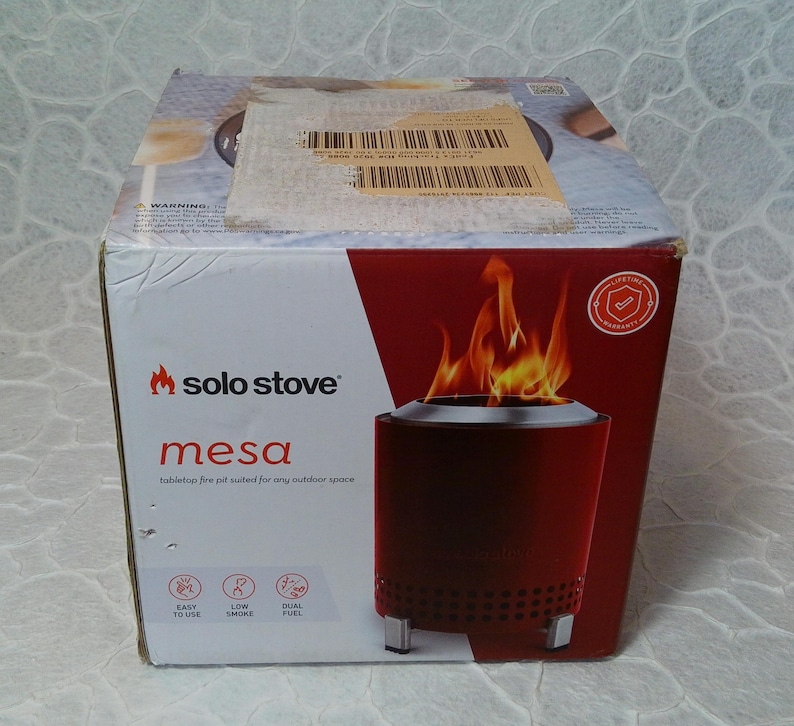 May include: A red Solo Stove Mesa tabletop fire pit in its original packaging. The box features the Solo Stove logo, product name, and a graphic of the fire pit with flames. The box also highlights features like easy use and low smoke.