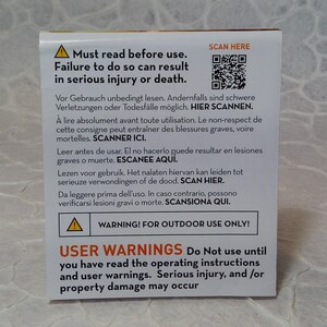May include: A white and yellow warning label with text in multiple languages. The label warns of serious injury or death if instructions are not followed. Includes a QR code and the text: "WARNING! FOR OUTDOOR USE ONLY!"