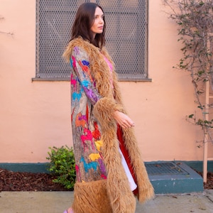 May include: A long, colorful coat with a faux fur trim and a pattern of horses. The coat is worn with a pink top, white dress, and lavender platform sandals. The coat's colors include brown, orange, blue, and yellow.