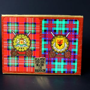May include: Two decks of playing cards with a tartan design. The cards feature the Stewart and MacDonell clan crests. The box reads "Plastic Finish Made in Britain."