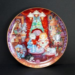 May include: A decorative ceramic plate featuring a whimsical illustration of cats enjoying tea time in a cozy, Victorian-style setting. The plate is decorated with intricate details, including a red velvet armchair, a floral arrangement, and a teapot. The cats are dressed in formal attire and hold teacups and a heart-shaped box that reads "Love".