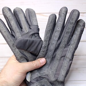 May include: A pair of grey gloves with suede detailing and perforated accents. The gloves feature a classic design with reinforced stitching and a secure fit. The gloves are made of a durable material and are suitable for various activities.