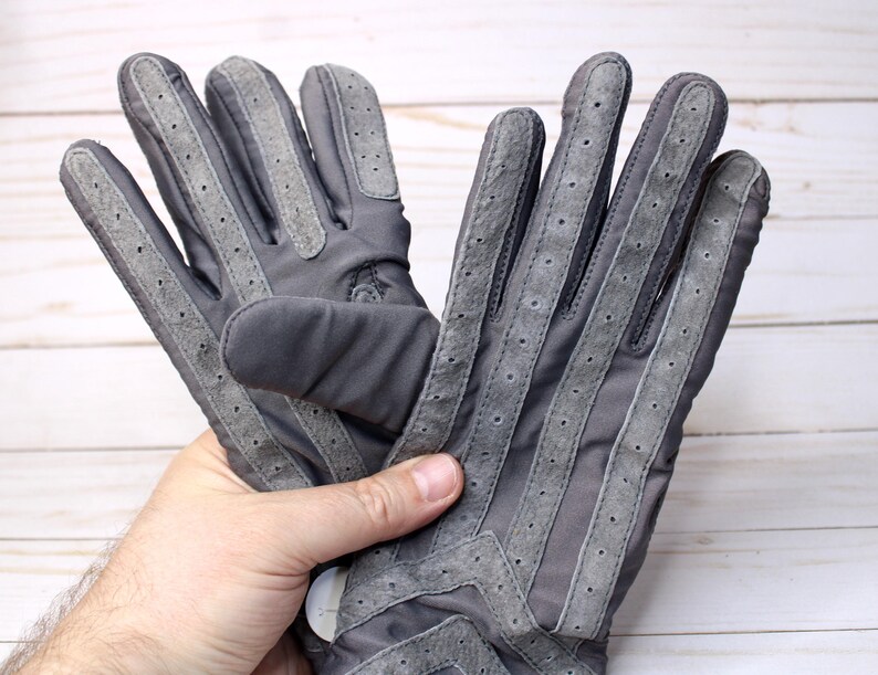 May include: A pair of grey gloves with suede detailing and perforated accents. The gloves feature a classic design with reinforced stitching and a secure fit. The gloves are made of a durable material and are suitable for various activities.