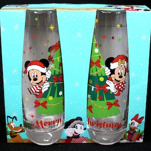 May include: Set of two clear glass champagne flutes with a Christmas tree and Mickey Mouse and Minnie Mouse designs. The glasses have the words "Merry" and "Christmas" printed on them.