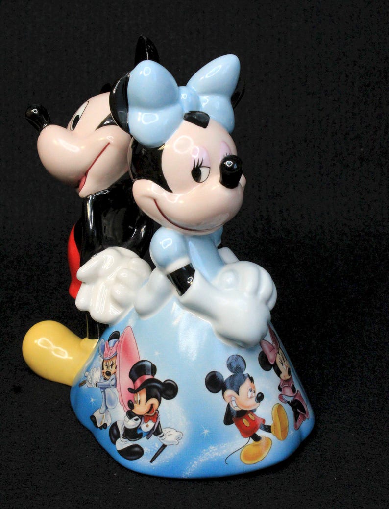 May include: A ceramic figurine of Mickey Mouse and Minnie Mouse. Mickey is wearing his signature red shorts and black shoes. Minnie is wearing a blue dress with a white bow. The figurine is decorated with a blue background and images of Mickey and Minnie in different poses.