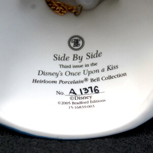 May include: White porcelain bell with a gold chain, featuring the text "Side By Side", "Third issue in the Disney's Once Upon a Kiss Heirloom Porcelain Bell Collection", "No. A 1376", "&copy;Disney", "&copy;2005 Bradford Editions", and "15-16839-003".