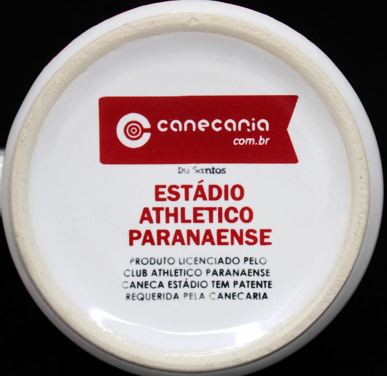 May include: White ceramic mug bottom with red text and logo. The text reads "EST&Aacute;DIO ATHLETICO PARANAENSE" and "canecaria.com.br". The mug is a licensed product of Club Athletico Paranaense.