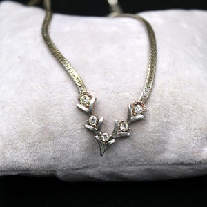 May include: A silver chain necklace with a silver pendant featuring a V-shaped design with five clear rhinestones.