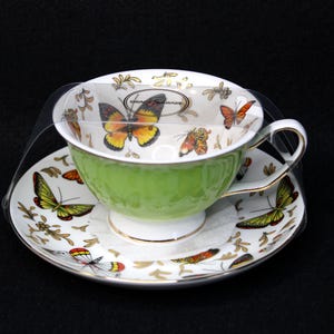 May include: A green teacup and saucer set with a butterfly design. The cup and saucer are decorated with colorful butterflies and floral accents.