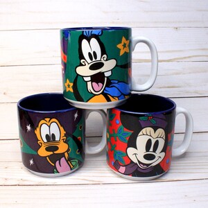 May include: Three ceramic mugs with holiday-themed designs featuring Mickey Mouse characters. The mugs are blue, green, and red with white accents. The first mug features Goofy wearing a Santa hat, the second mug features Pluto wearing a Santa hat, and the third mug features Minnie Mouse wearing a Santa hat.