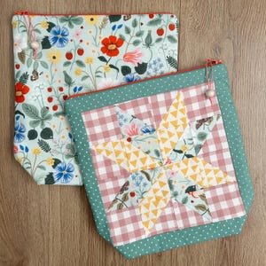 May include: Two square zippered pouches. One features a light blue background with a colourful floral and strawberry print. The other displays a central star pattern made of yellow and floral fabric, set against a pink gingham background with a green border.
