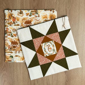 May include: Two square fabric pouches with zip closures and wooden bead pulls. One pouch features a repeating pattern of woodland creatures in a forest setting. The other displays a central star quilt block design with a mouse illustration.