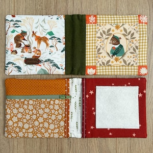 May include: A fabric organizer featuring a forest-themed print with bears and deer, a central olive green panel, and a patchwork section with a bear illustration. The reverse side includes a zippered pocket with floral patterns and a white felt square.