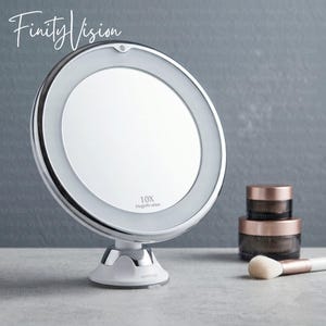 May include: A white and silver vanity mirror with a circular design and a 10X magnification feature. The mirror is on a white base with a silver accent. Makeup jars and a brush are next to the mirror.