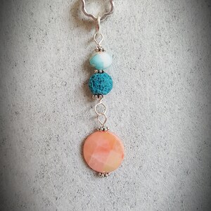 May include: A silver chain necklace with a flower-shaped pendant and three beads. The beads are a light blue, dark blue, and a pink and white round bead.