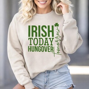 May include: A beige sweatshirt with the text "IRISH TODAY HUNGOVER" in green block letters. The word "Tomorrow" is written vertically in a script font, with a green shamrock. The sweatshirt is a casual style.