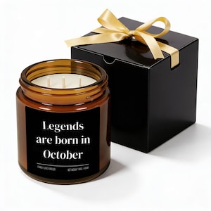 May include: A brown glass candle jar with three wicks and a black label that reads "Legends are born in October." The candle sits next to a black gift box tied with a gold ribbon. The candle weighs 16 oz / 454g.