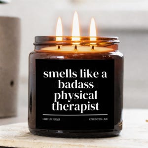 May include: A lit three-wick candle in a brown glass jar. The black label reads "smells like a badass physical therapist." The candle is labeled "Family Love Forever" and weighs 16 oz / 454g.