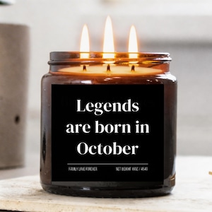 May include: A lit candle in a brown glass jar with a black label. The label reads "Legends are born in October." The candle has three wicks and is labeled "Family Love Forever" and "Net Weight 16oz / 454g."