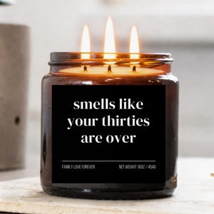 Puede incluir: Vela encendida de tres mechas en un tarro de cristal marr&oacute;n. La etiqueta negra dice "smells like your thirties are over". La etiqueta tambi&eacute;n dice "FAMILY LOVE FOREVER" y "NET WEIGHT 16OZ / 454G."