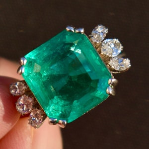 Op de afbeelding: Een vierkante smaragden ring gezet in witgoud met een halo van kleinere diamanten.