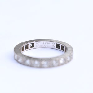 May include: A silver band ring with small diamonds set in the band. The inside of the band is engraved with 'AM 8568 750 53'.