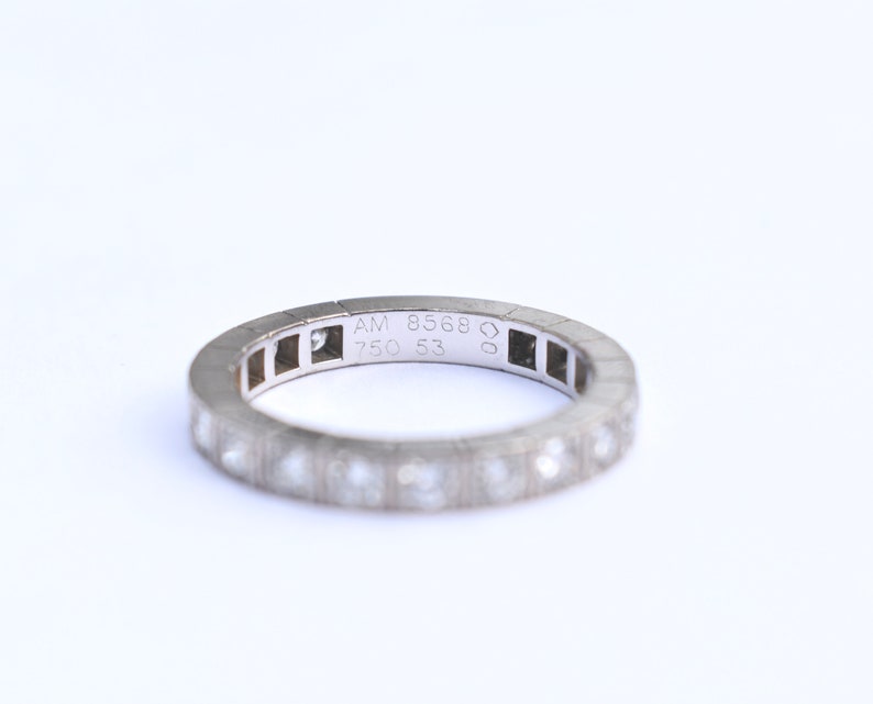 May include: A silver band ring with small diamonds set in the band. The inside of the band is engraved with 'AM 8568 750 53'.