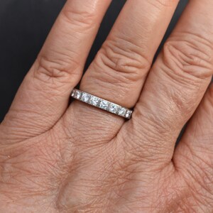 May include: A silver eternity band with a row of small, square-shaped diamonds.