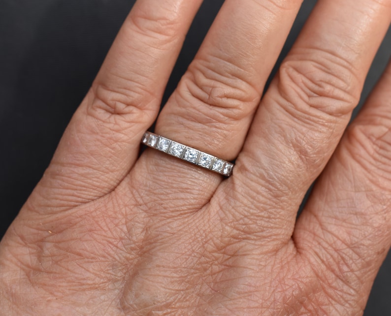 May include: A silver eternity band with a row of small, square-shaped diamonds.