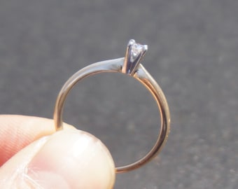 May include: A simple gold band ring with a single, small, clear diamond set in a prong setting.