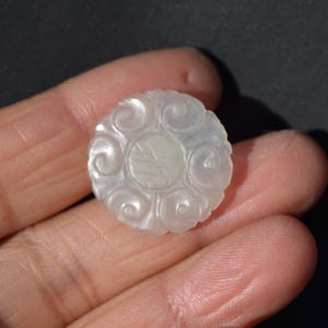 May include: A white jade pendant with a carved floral design. The pendant is round and has a smooth, polished surface.