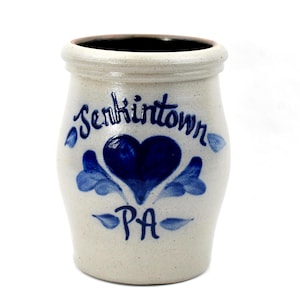 May include: A cream-coloured stoneware crock with a dark interior. The crock features the word "Jenkintown" in script, a blue heart, and the letters "PA" in blue. The design is hand-painted.