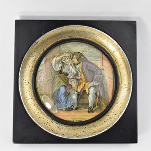 Puede incluir: Una obra de arte ovalada enmarcada con un marco dorado. La obra representa a un hombre y una mujer en una habitación con una ventana. El hombre lleva una chaqueta morada y la mujer lleva un vestido azul. La obra se titula "Uncle Toby".