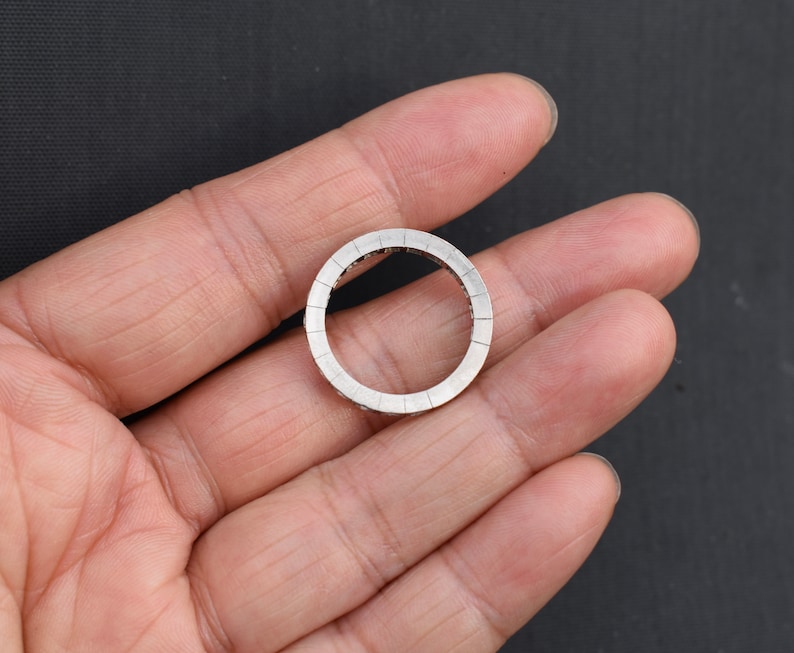 May include: A silver ring with a round design. The ring is set with small, clear stones that create a sparkling effect.