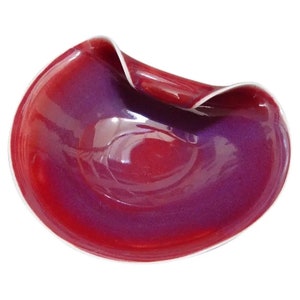 Puede incluir: Un cuenco de cerámica rojo y morado con un diseño ondulado único. El cuenco está esmaltado y tiene un acabado brillante.