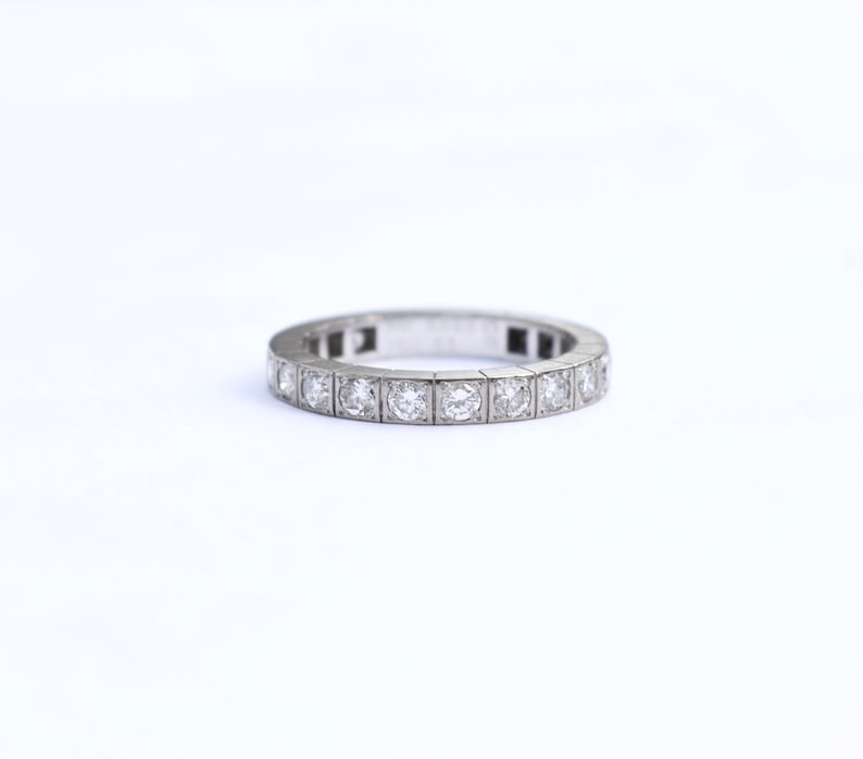 May include: A silver band with a row of small, round, clear diamonds set in square prongs.