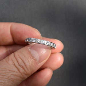 May include: A silver band with a row of small, square-shaped diamonds.