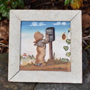 Peut inclure: Une œuvre d'art encadrée et peinte à la main représentant un enfant postant une lettre dans une boîte aux lettres. L'œuvre présente un cadre de couleur claire, un ciel bleu avec des nuages et un tournesol. La boîte aux lettres porte le mot "Posta".