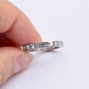 May include: A silver band ring with small diamonds set in the band and the word 'Cartier' engraved on the band.